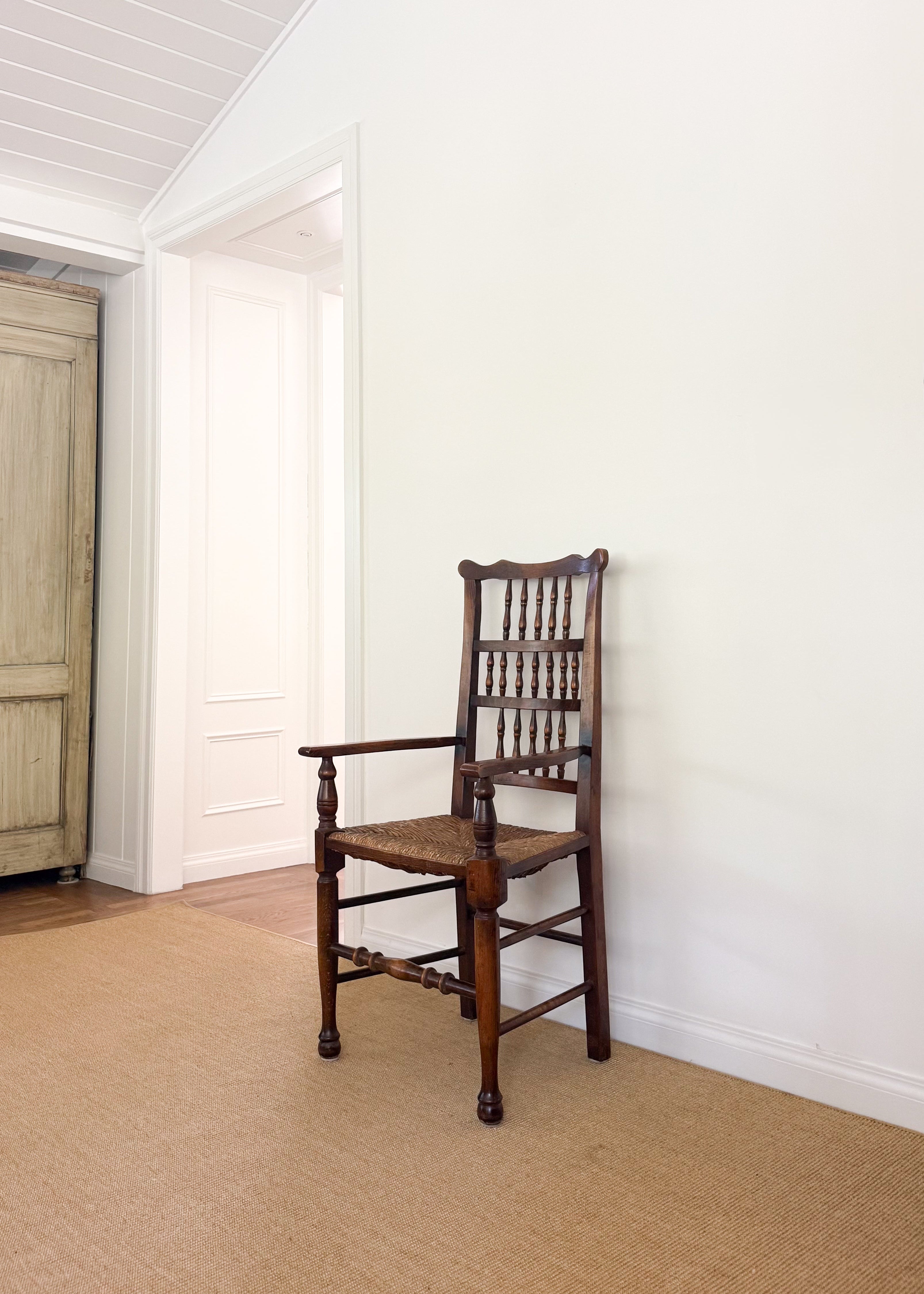 Antique wood chair against a white wall in a room with wooden flooring.