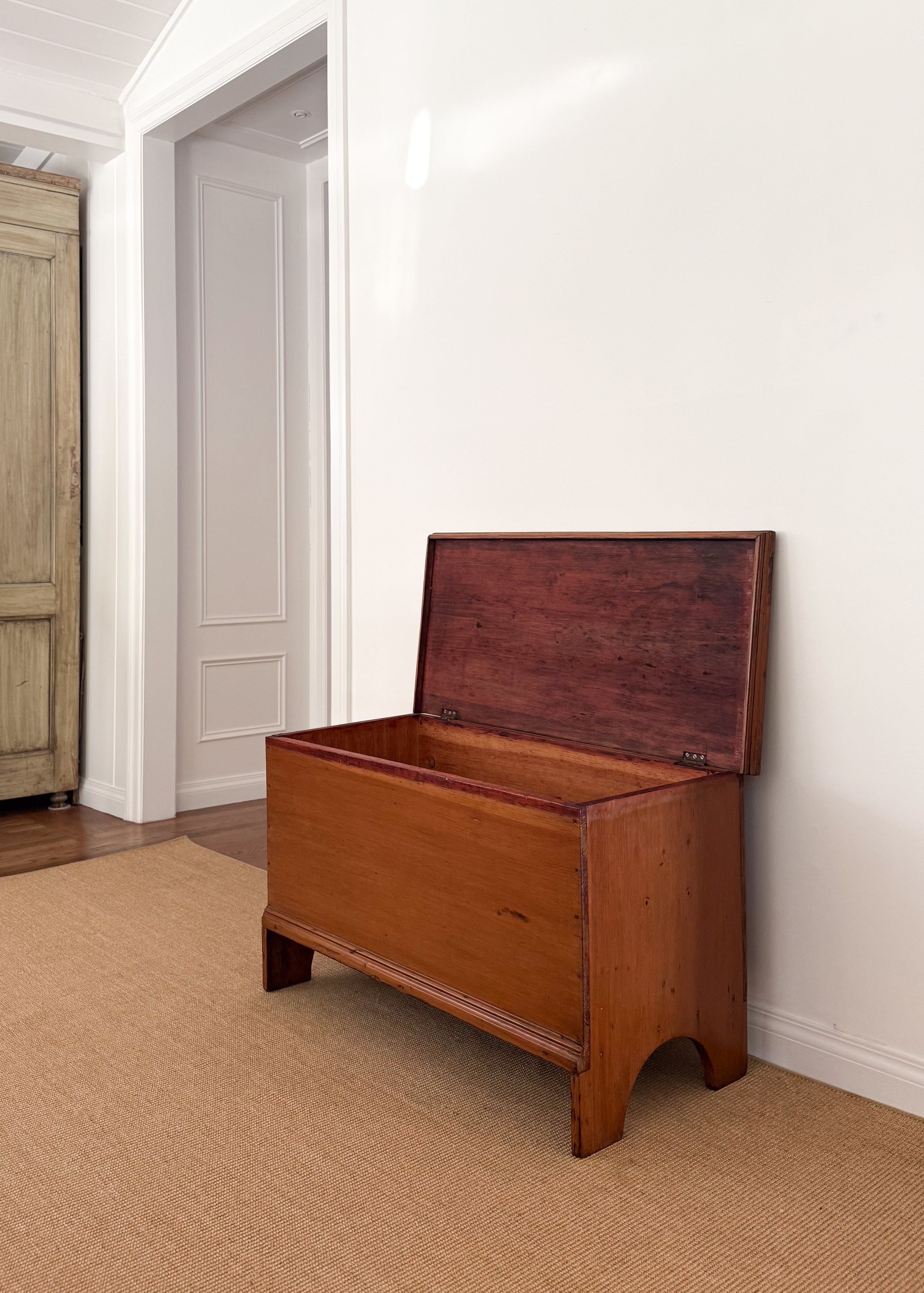 Antique wood chest in a room with a white wall and wooden floor.