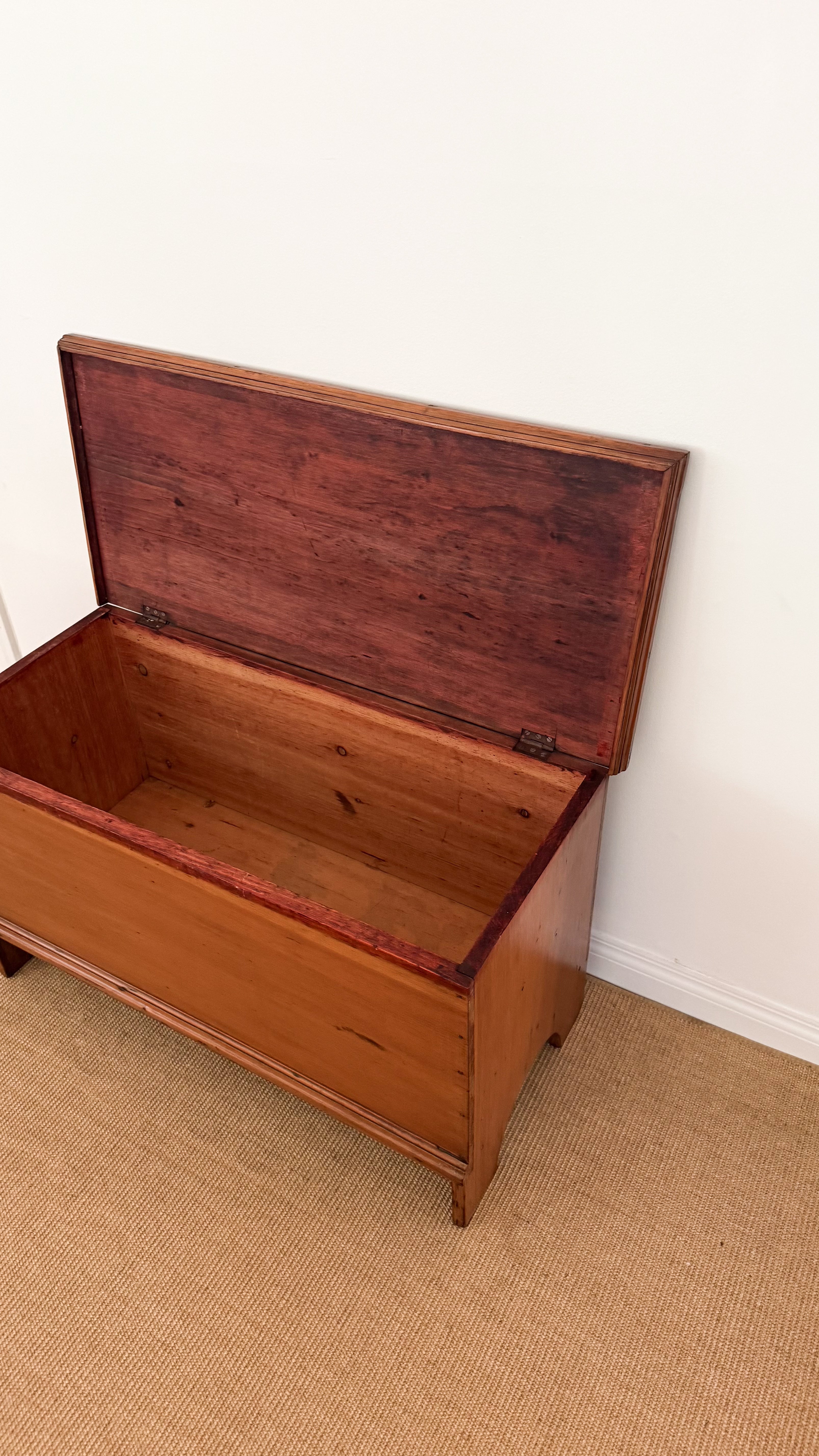 Antique wooden chest with open lid on a beige carpet against a white wall