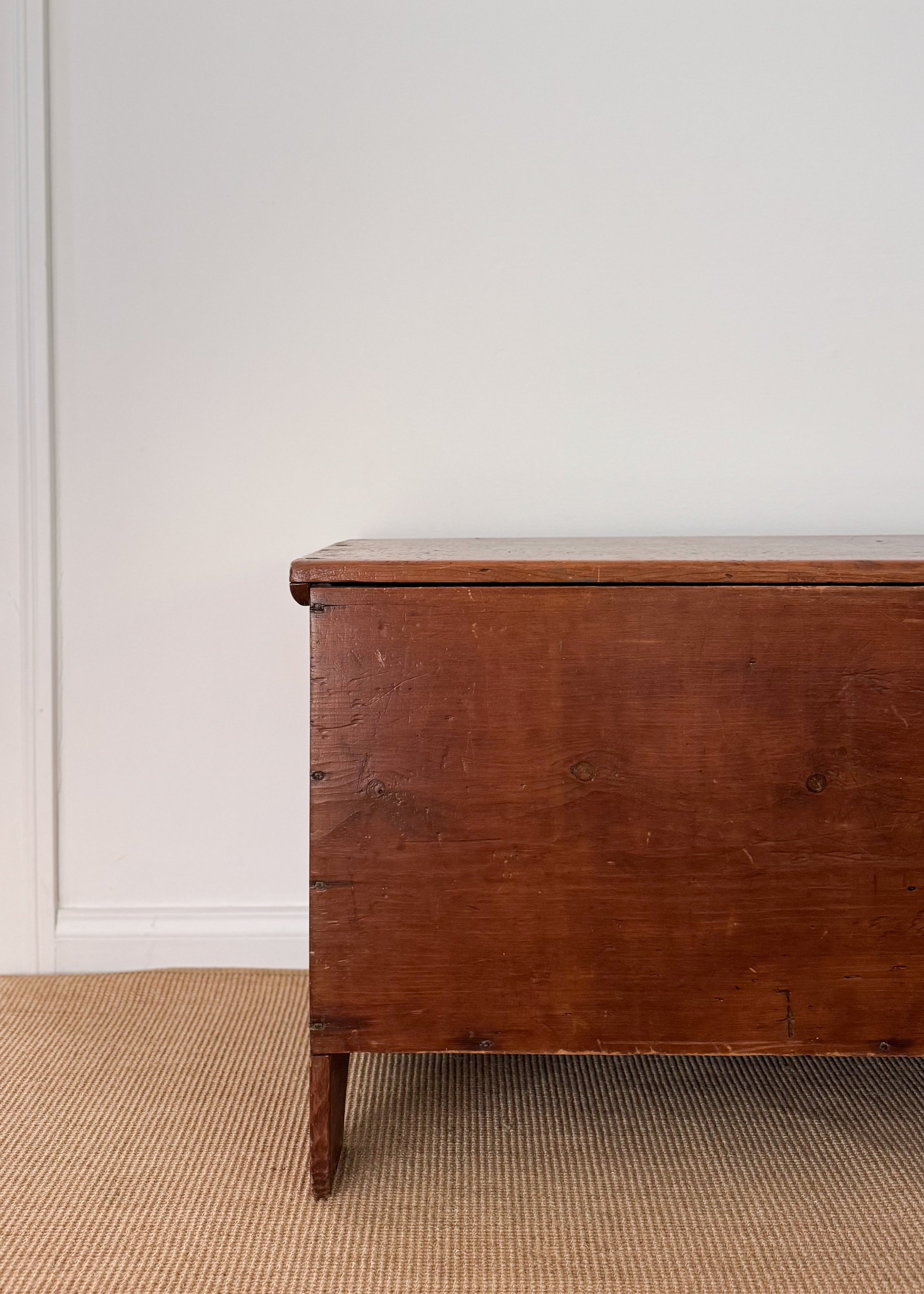 Up close to the left side of the Antique Early 19th century American Blanket Chest, placed ontop of beige carpeting.