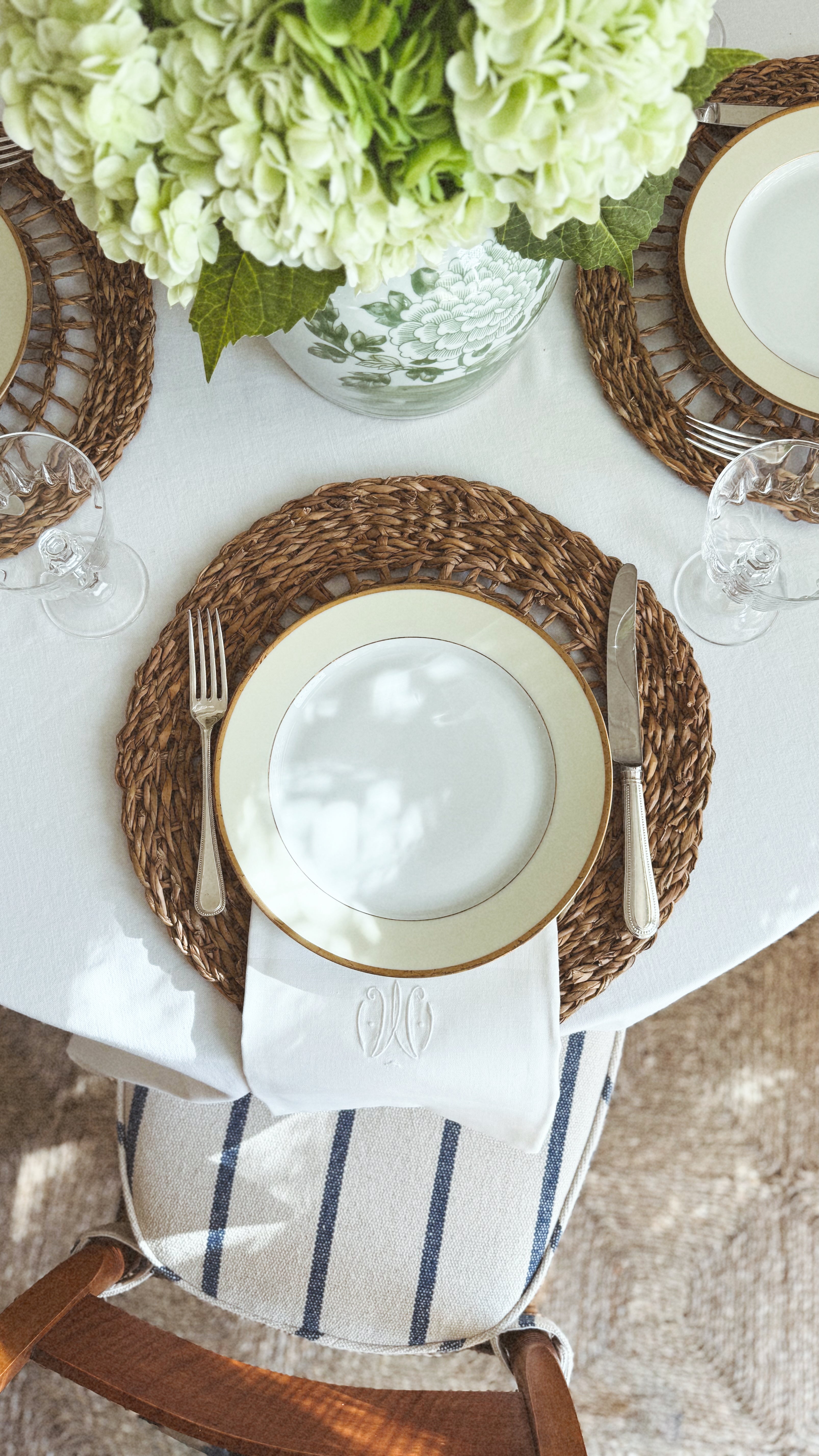 A gold rimmed plate and Vintage English Knife and dinner fork on a Seagrass placemat, with a striped napkin to the side, on a table setting
