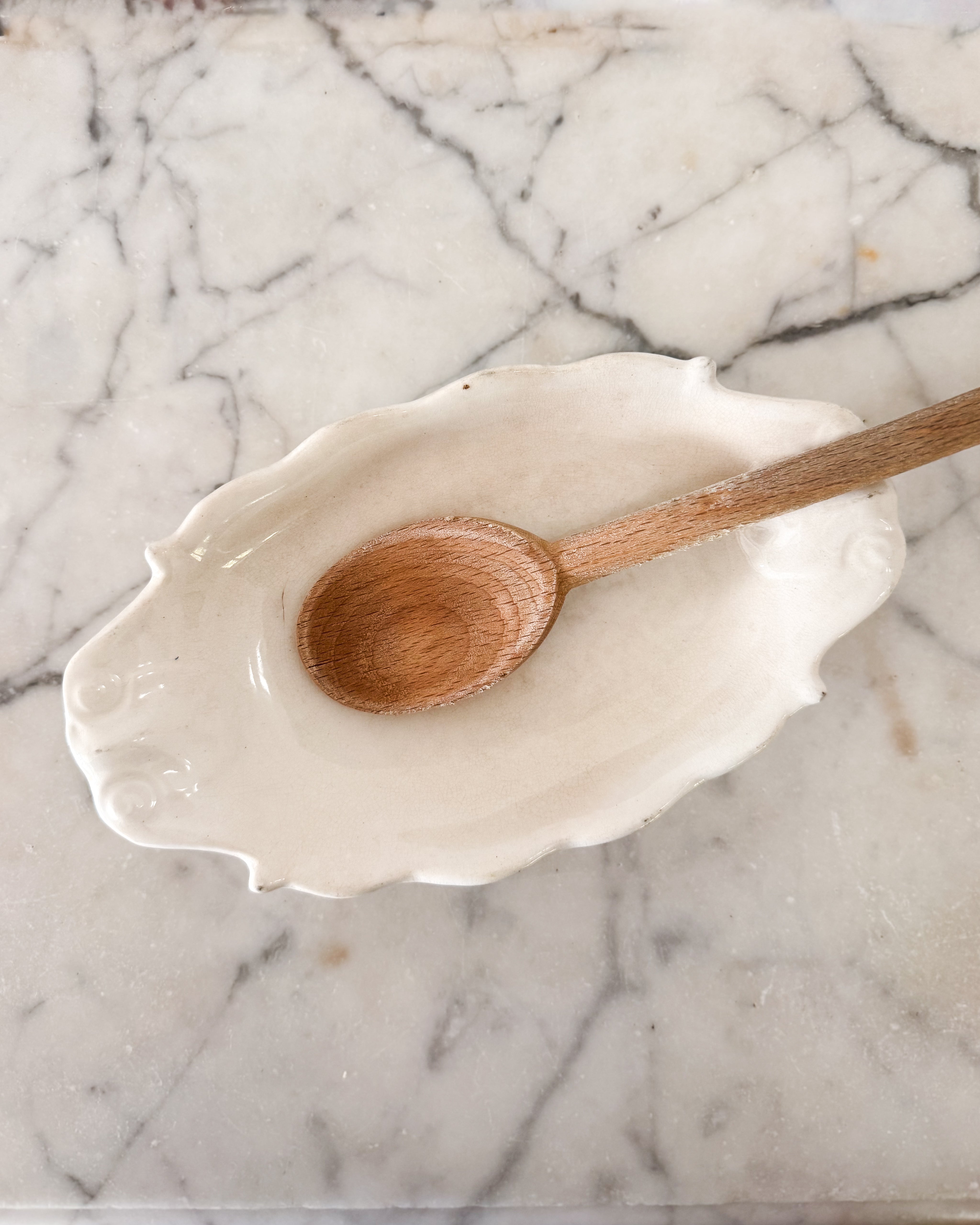 A vintage creamy white ironstone English spoon rest with a vintage wood cooking spoon.