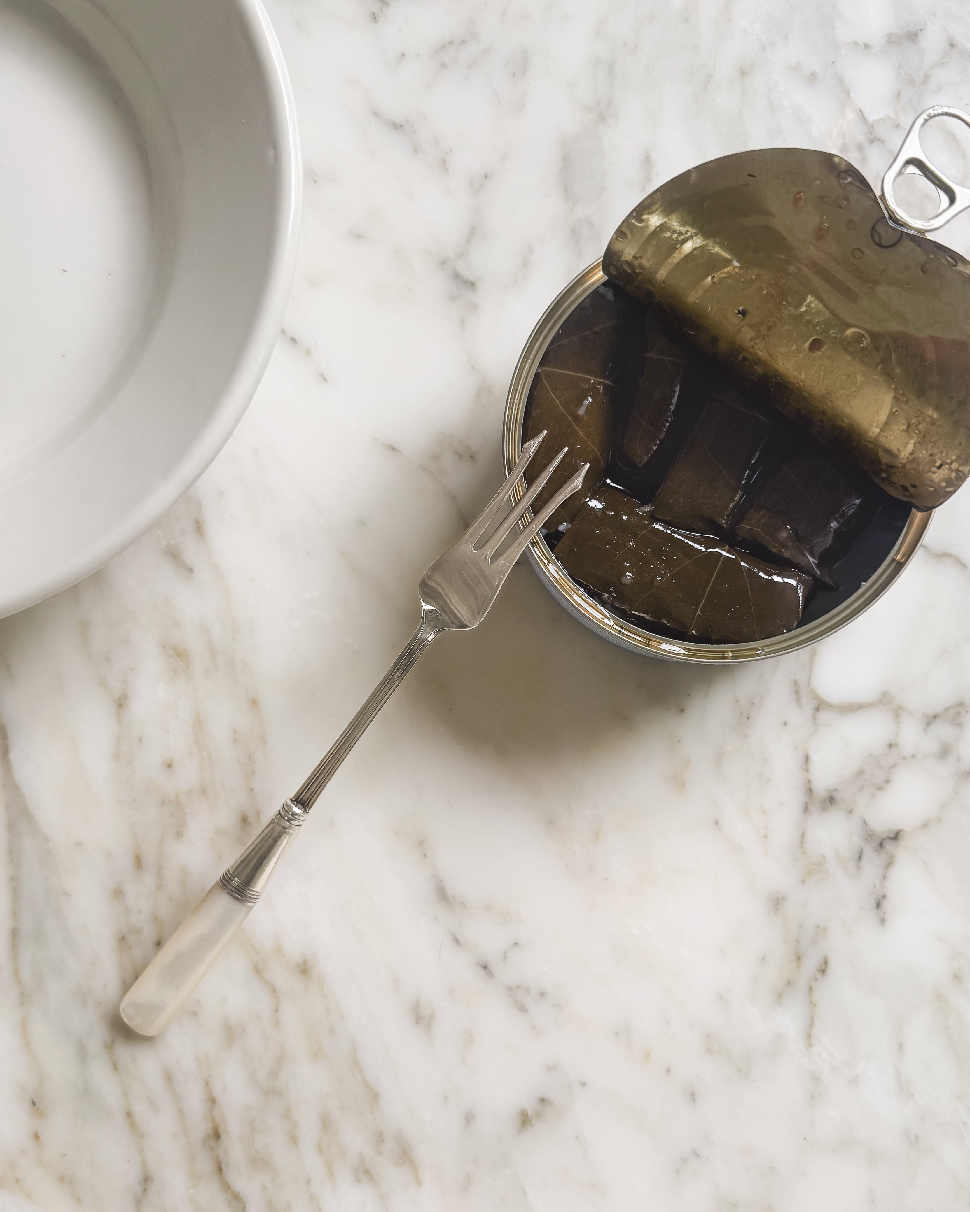 An open can of appetizers with an antique mother of pearl and sterling pickle fork.