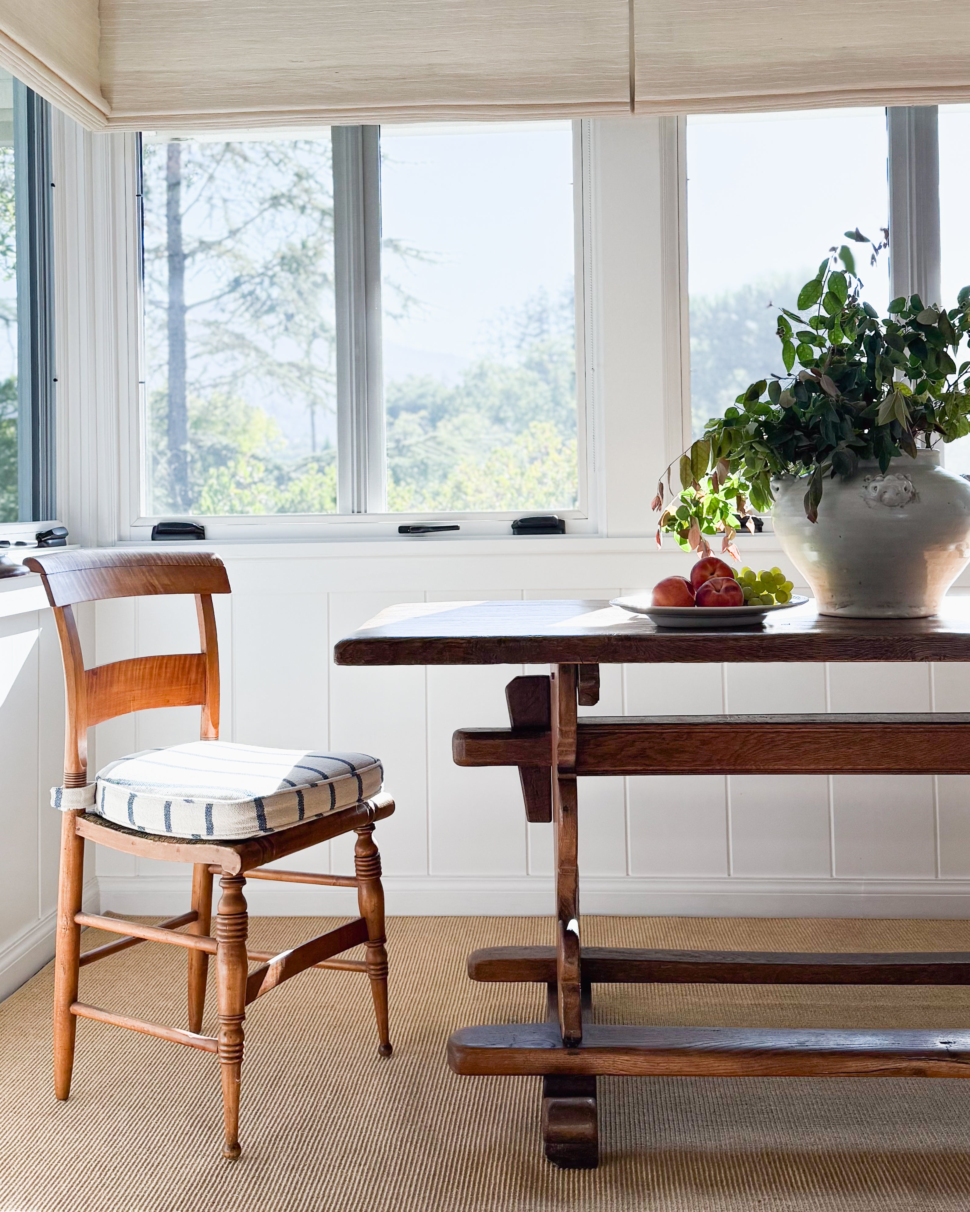 A McConnell white, handmade ceramic estate vessel with lion head accents. The vessel is full of branches on top of an antique trestle dining table.