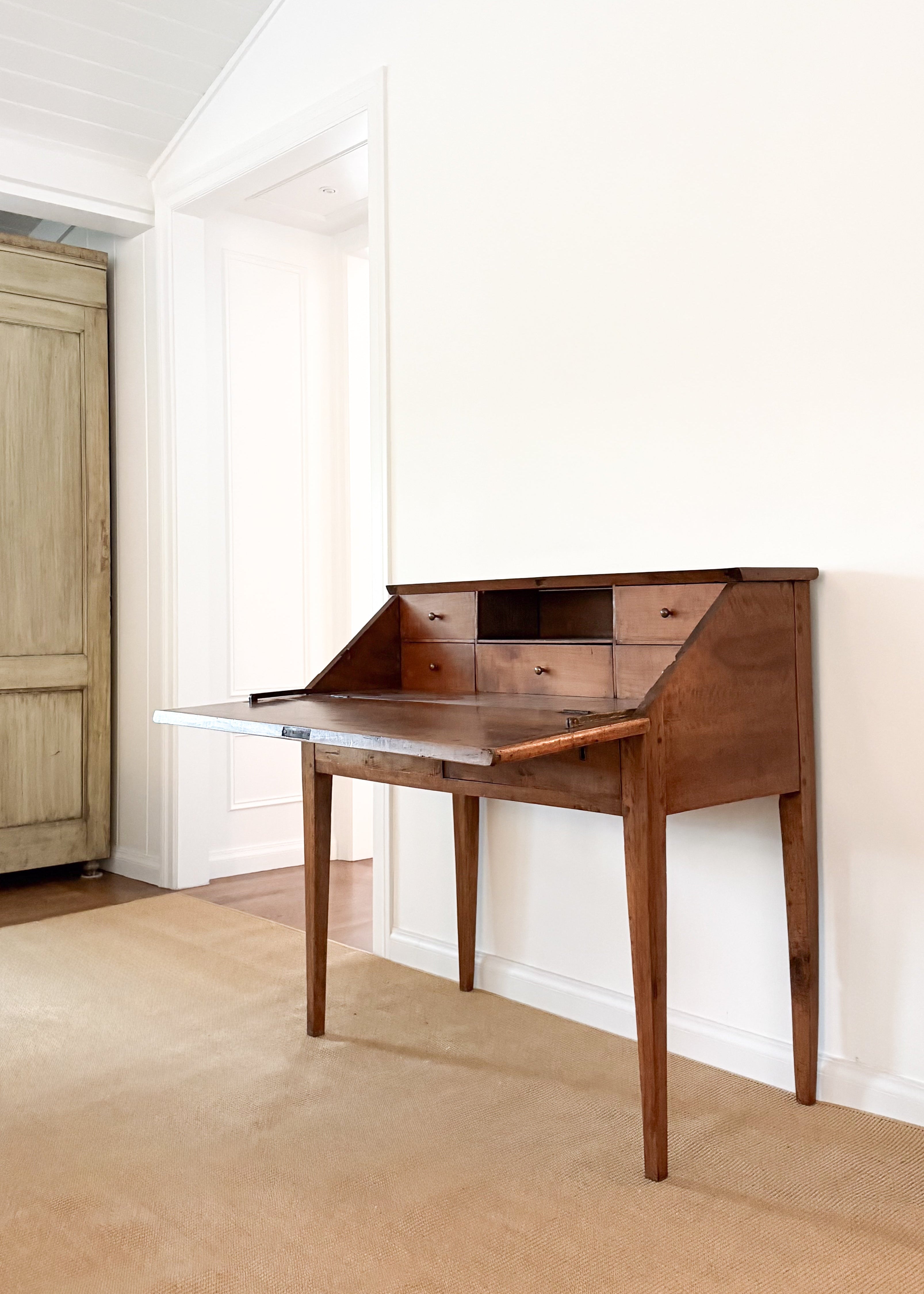 Antique wooden desk in a room with a white wall and wooden floor.
