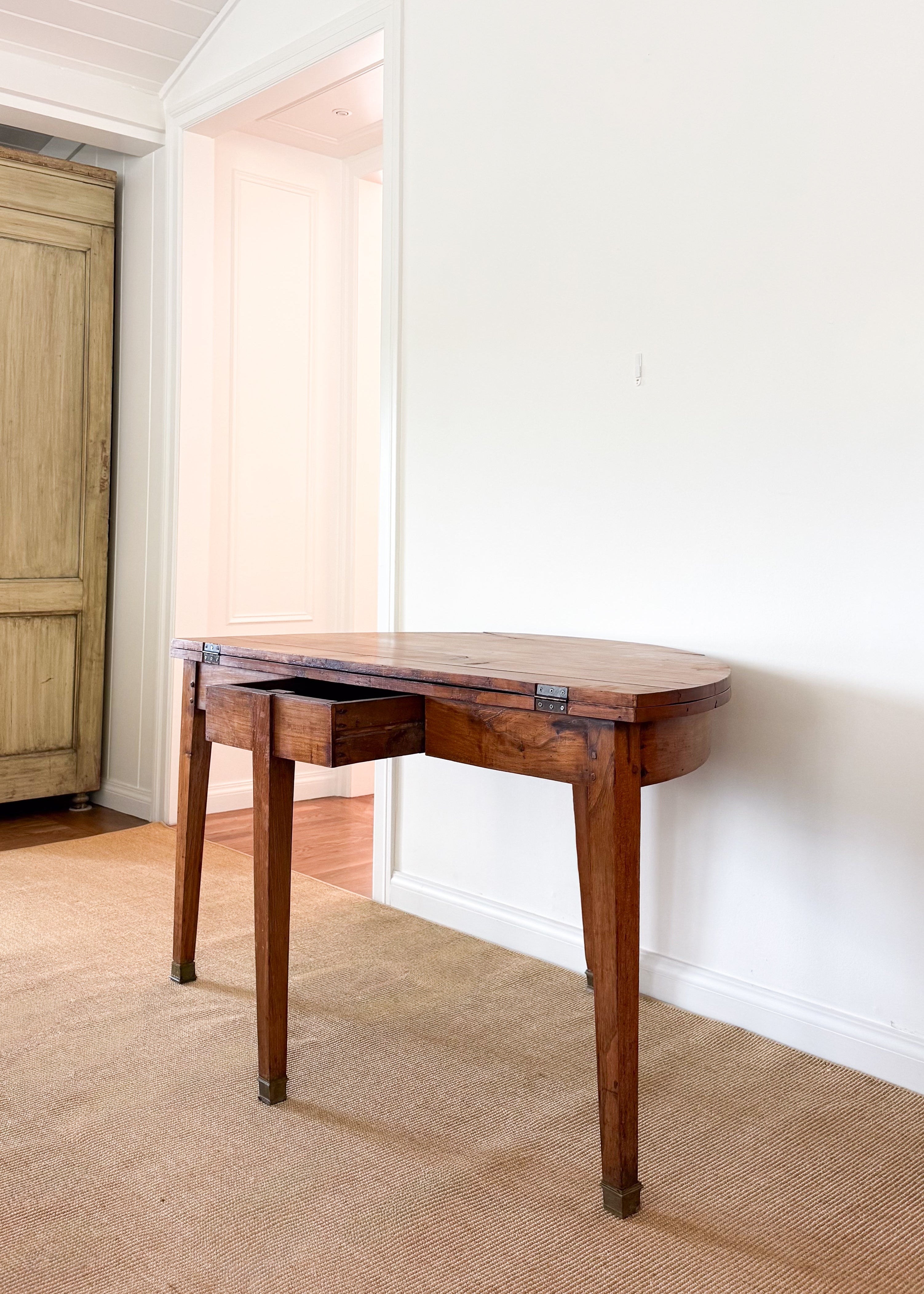 Antique wooden dining table against a white wall in a room with a wooden floor.