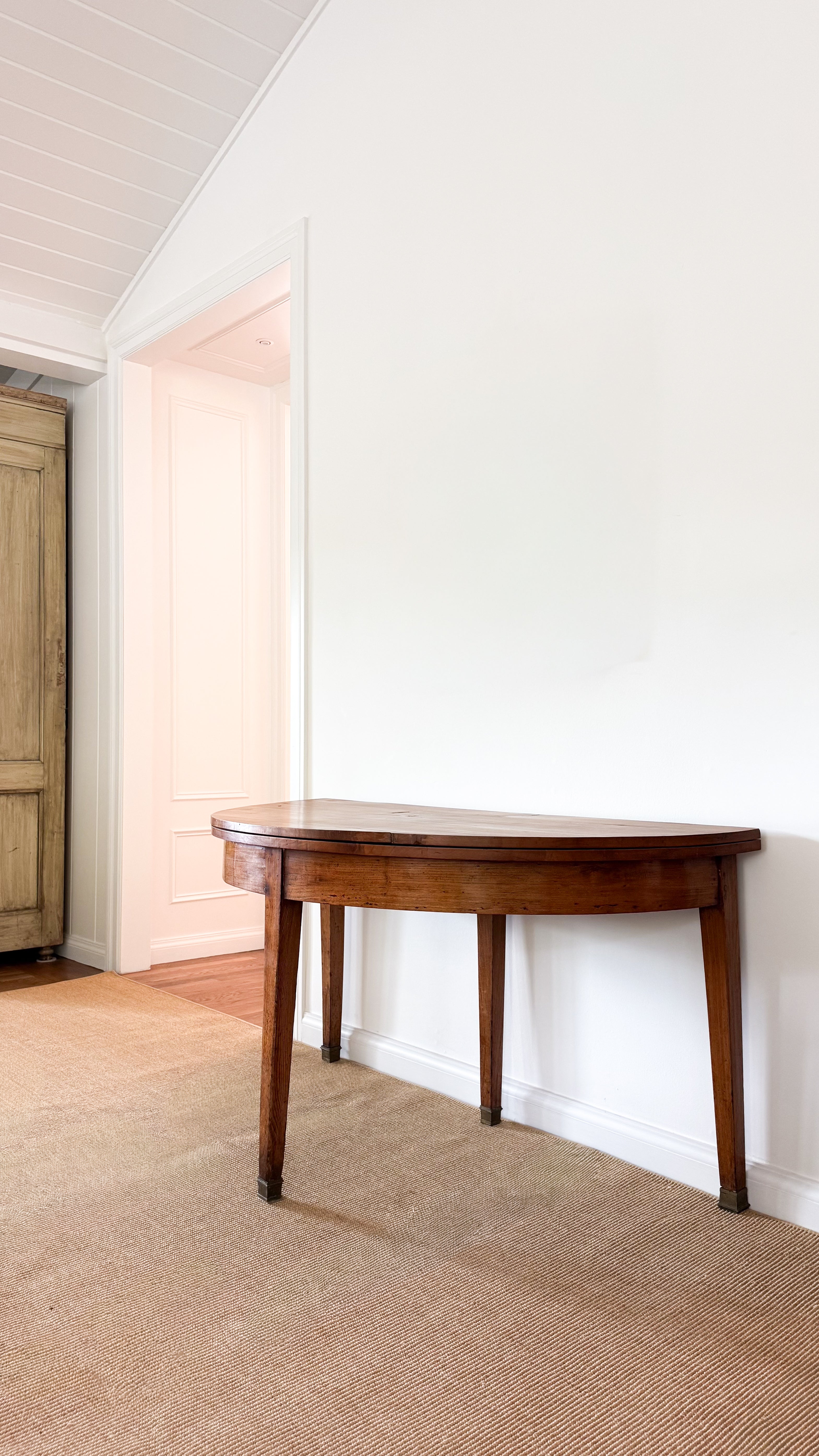 Antique wooden dining table against a white wall in a room with a wooden floor.