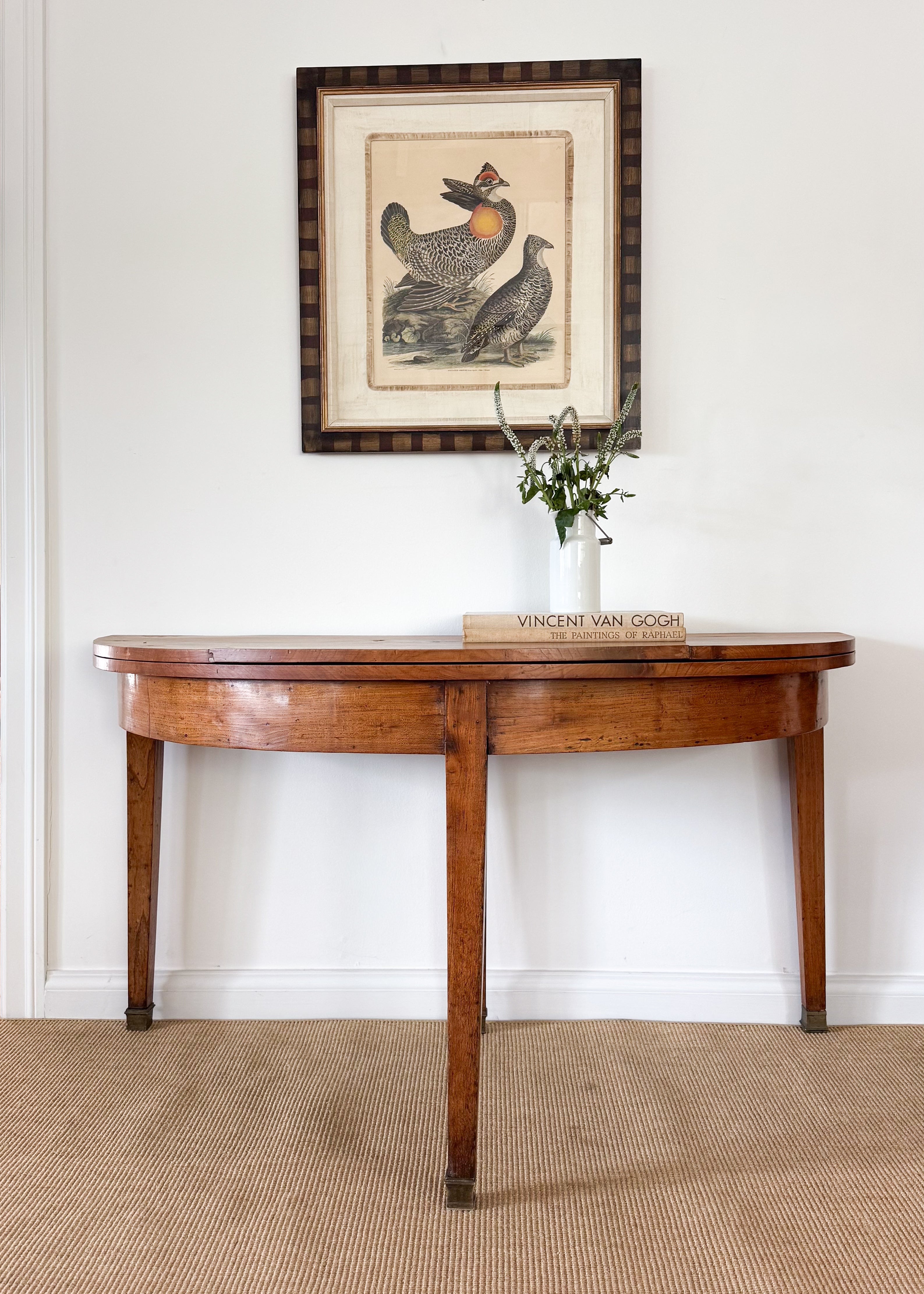 Wooden side table with a vase and framed picture on a white wall.