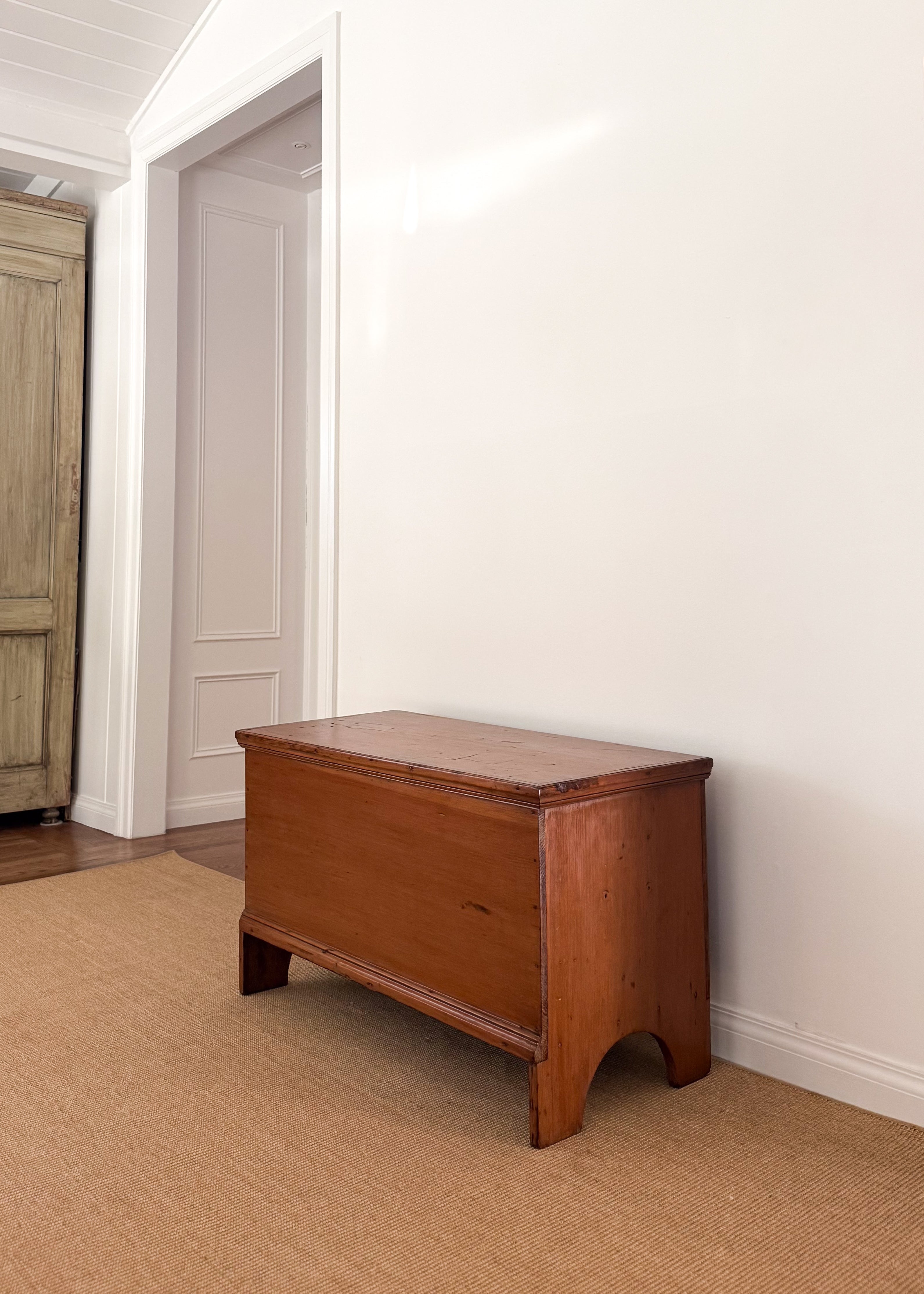 Antique wooden chest against a white wall in a room with carpeted floor.