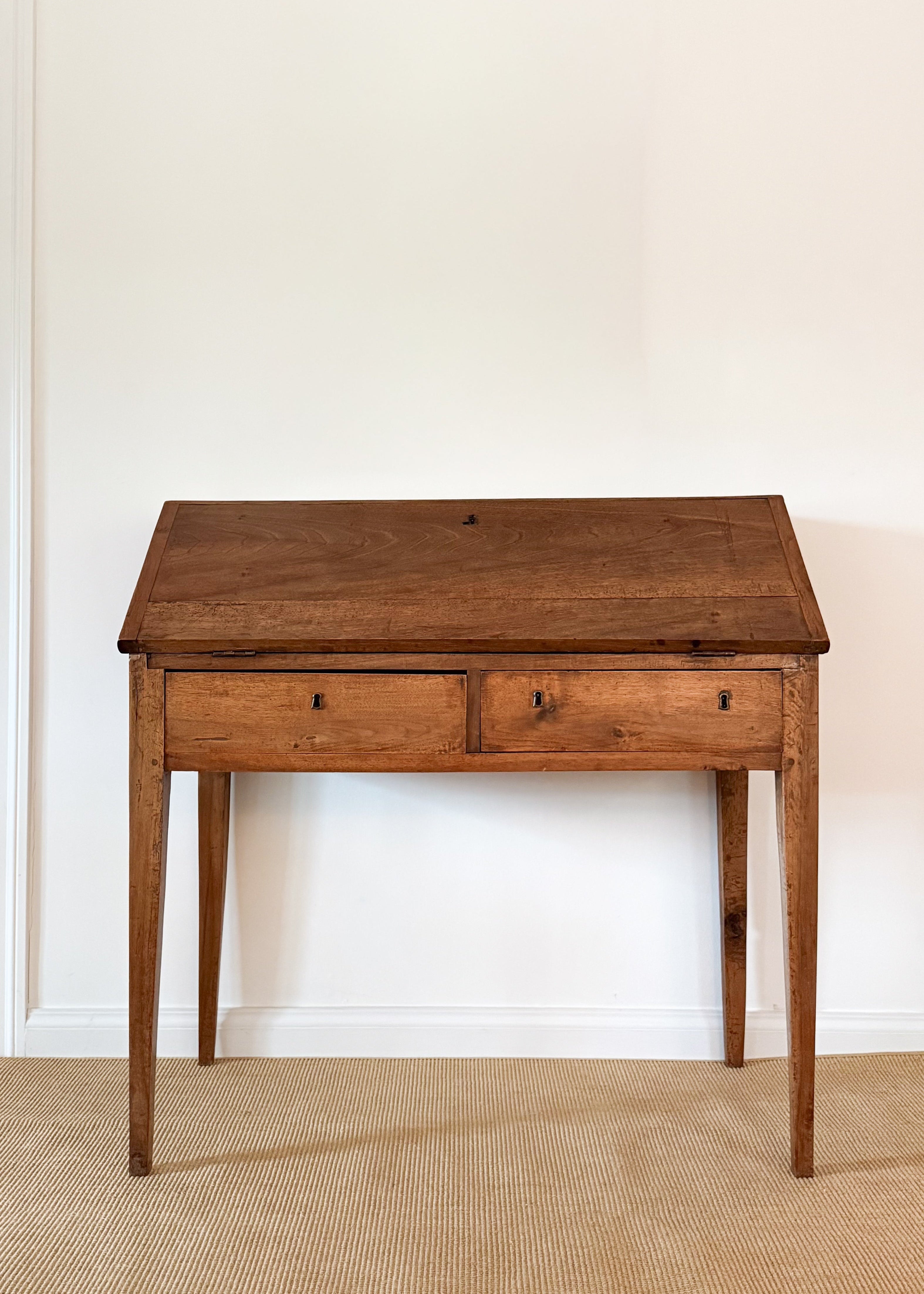 Antique wood desk with two drawers against a white wall