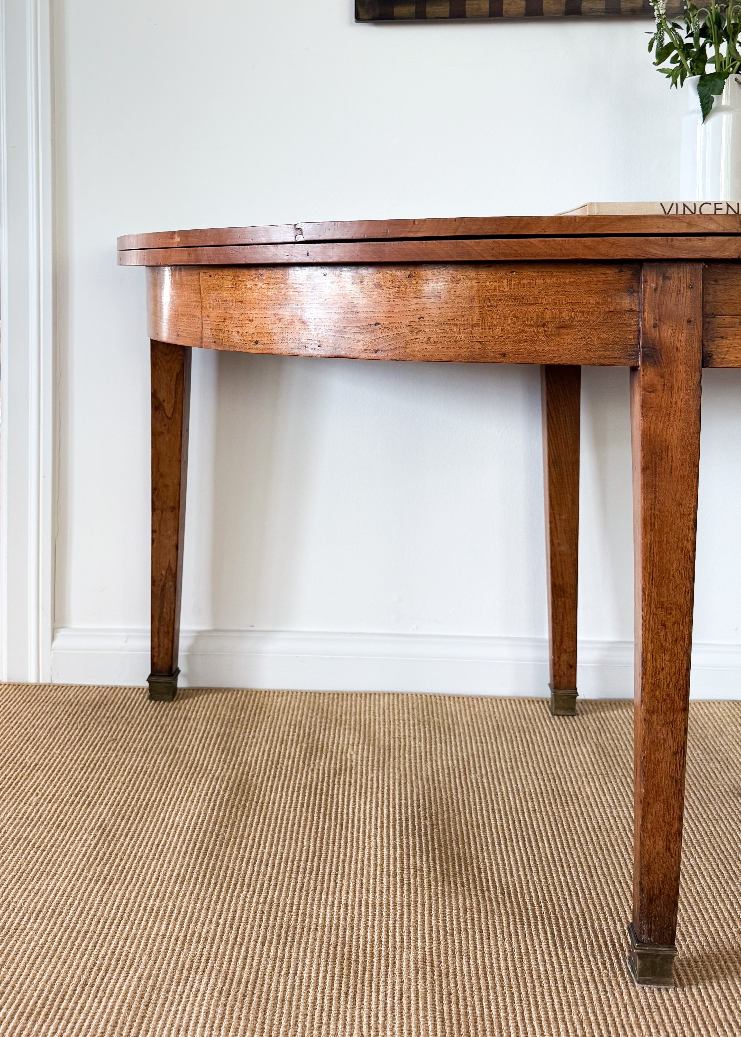 Antique wooden table against a white wall with a plant in the corner
