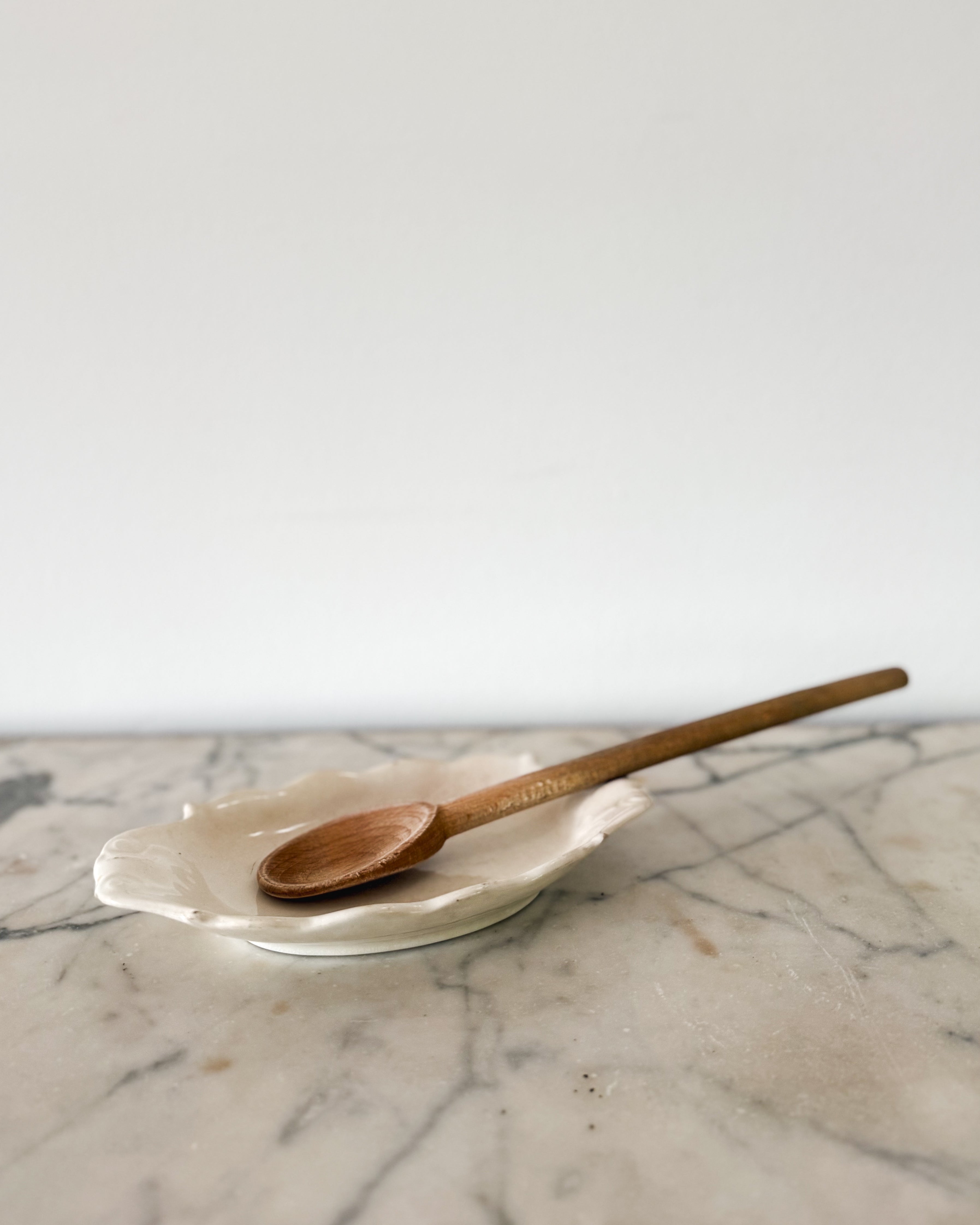 A creamy white English spoonrest with scrolled decorative details. Pictured with a vintage wood cooking spoon. 