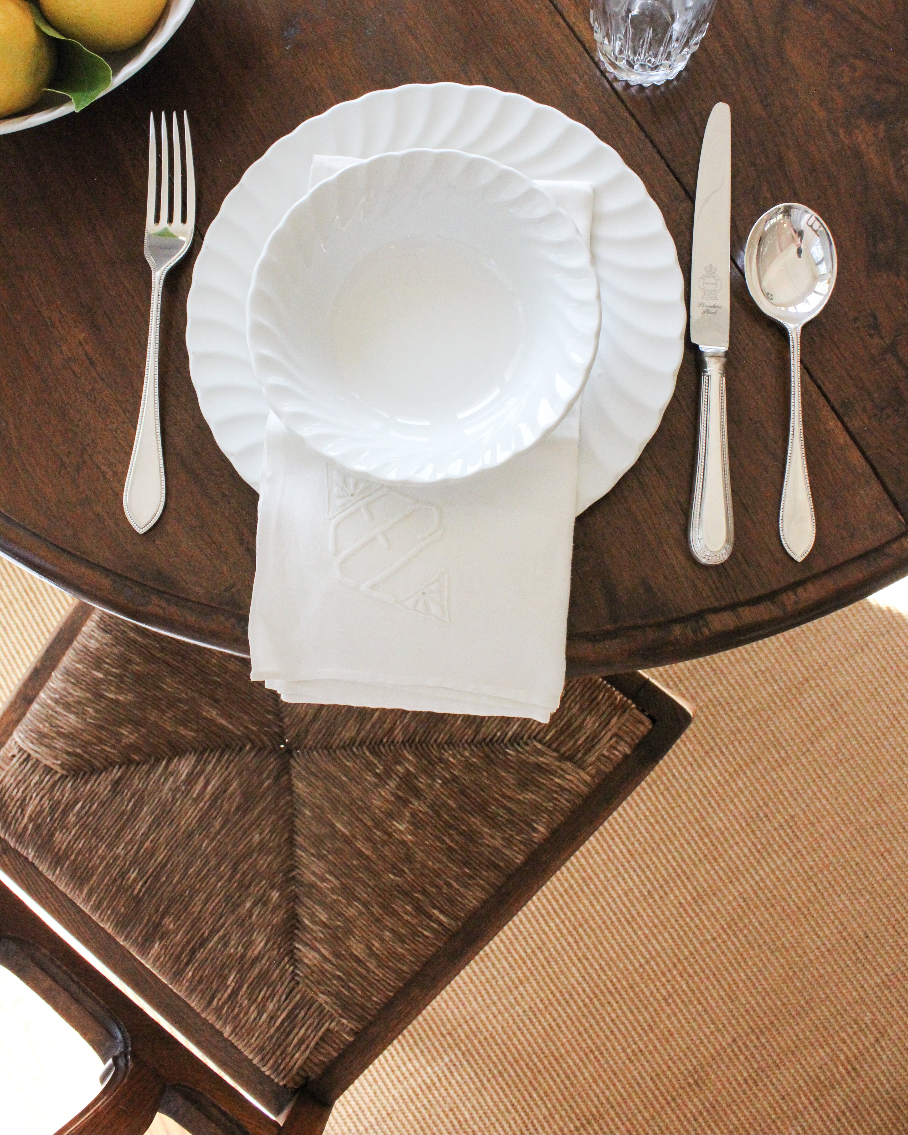 Vintage dining table with Rush Oak Seat, table setting with white plates, Vintage English Flatware, and a white scalloped bowl of lemons.