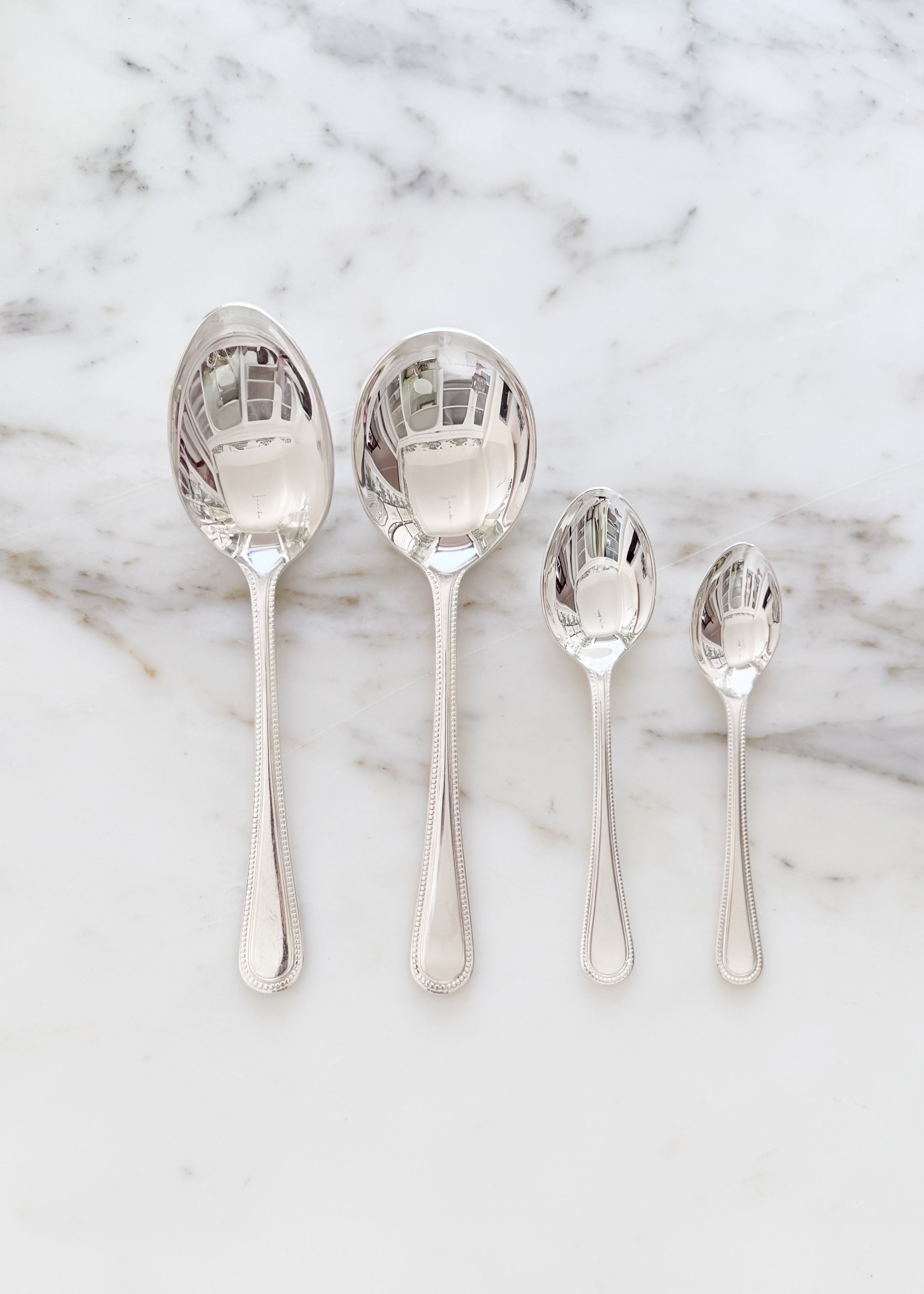 Vintage English tablespoon, soup spoon, teaspoon, and demitasse spoon on a marble background.