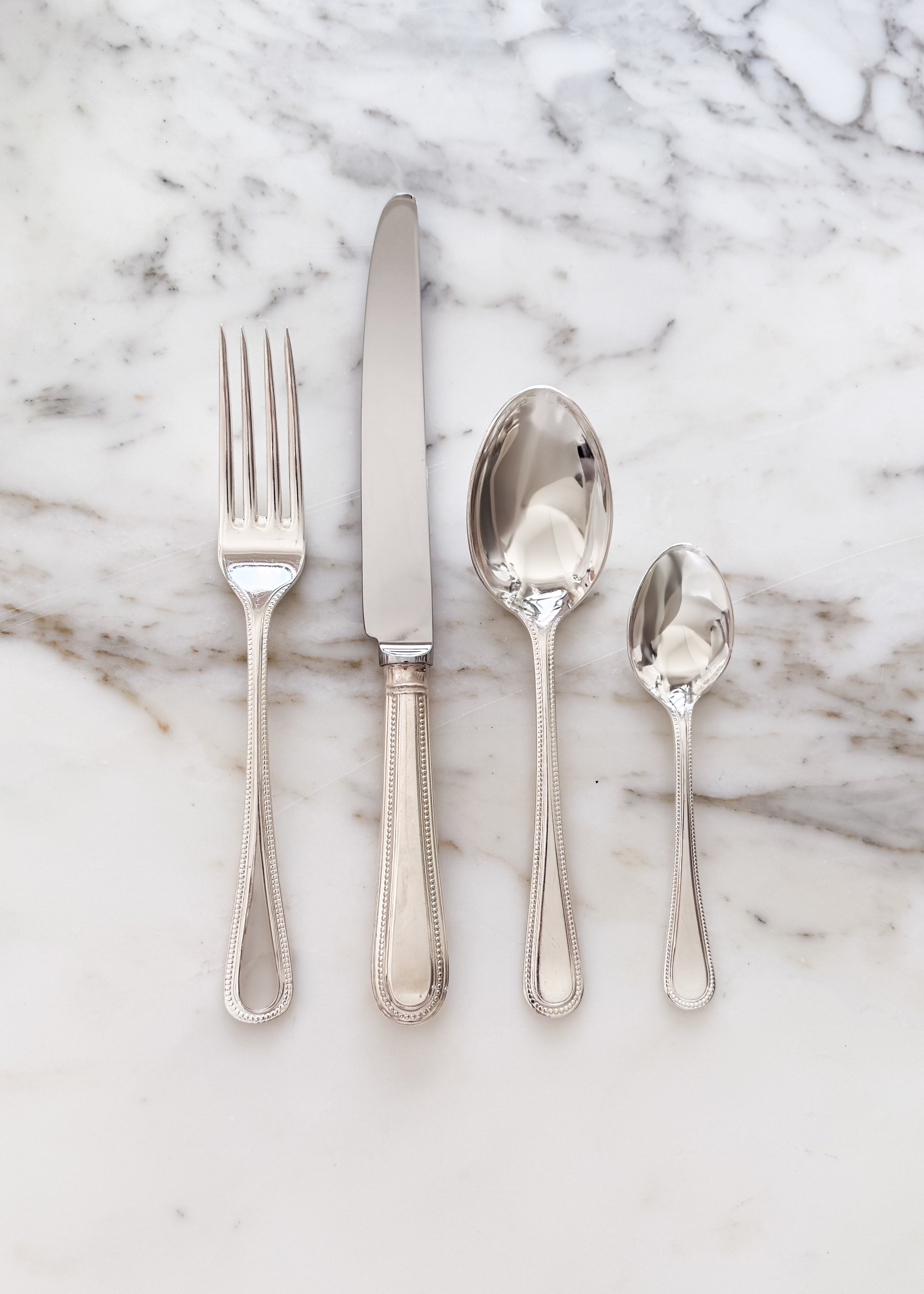 Vintage English cutlery including a dinner fork, knife, tablespoon, and teaspoon on a marble surface.