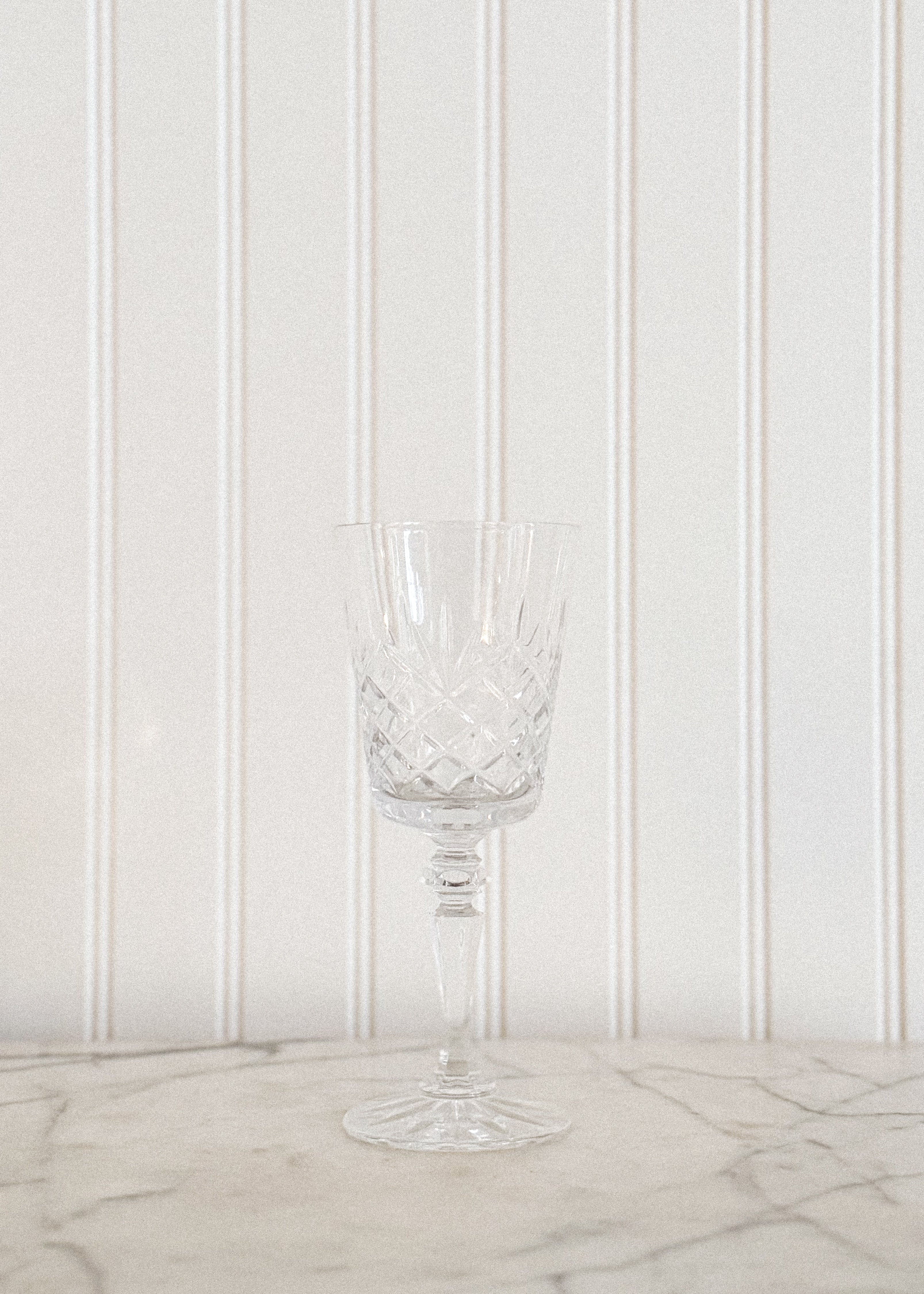 One Vintage Irish Cut Crystal Goblet standing on a marble countertop, in front of a white panel wall.