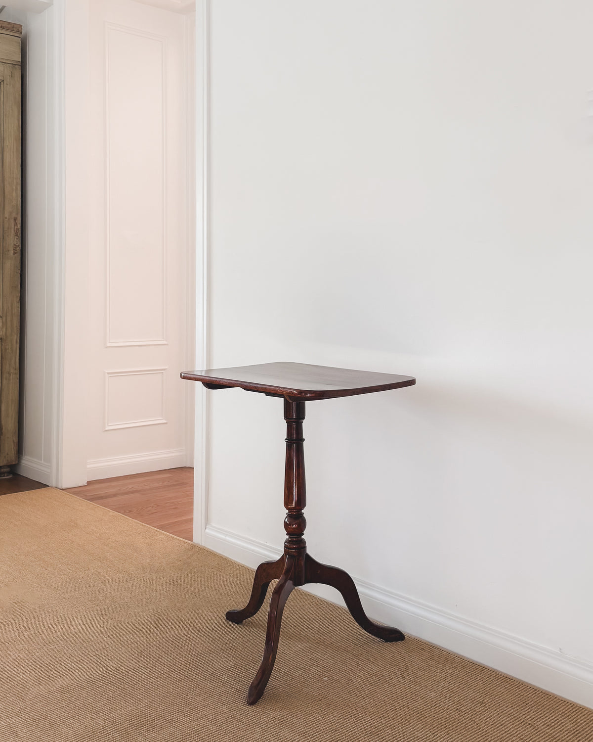 Angled view of an antique mahogany tilt-top table with slender tripod base and turned pedestal