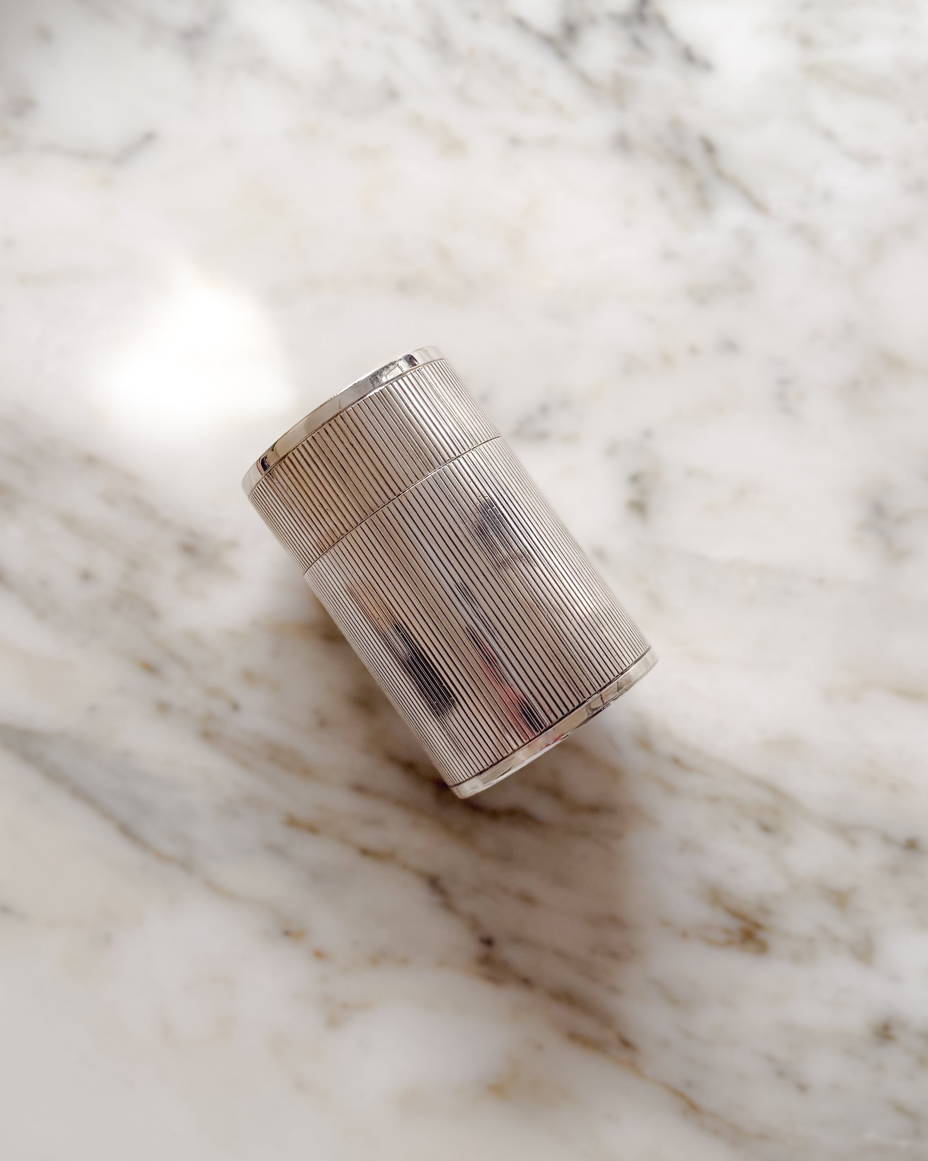 Vintage European silver-plated canister with finely fluted detailing resting on a white marble surface.