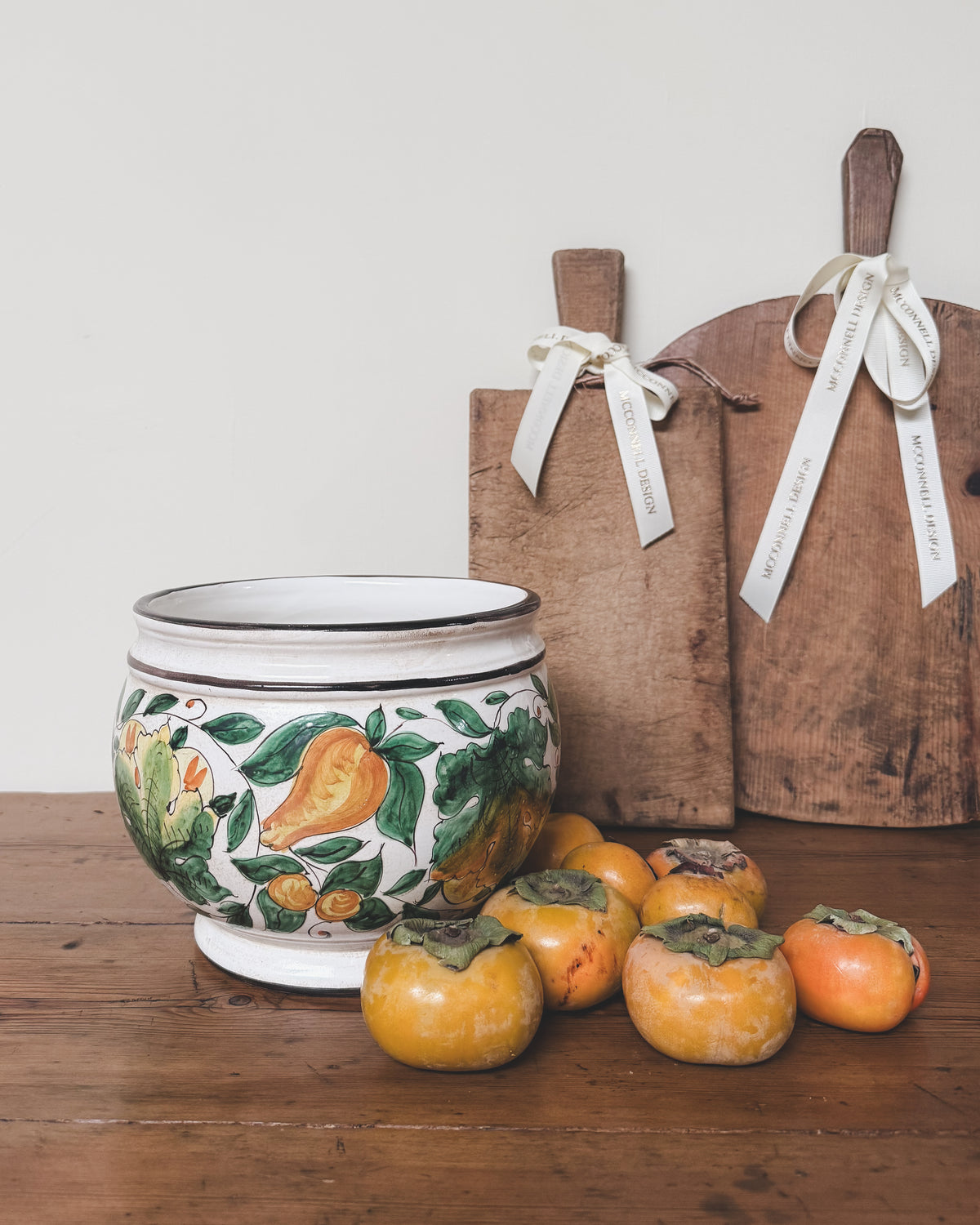 Vintage Italian hand-painted ceramic jardiniere styled with persimmons and antique European bread boards.